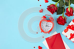 Flat lay photo of red roses, envelope with letter, gift box, hearts and alarm clock