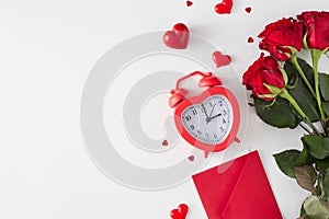 Flat lay photo of red roses, heart shaped alarm clock, envelope, hearts on white background