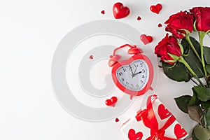 Flat lay photo of red roses, heart shaped alarm clock, gift box, hearts