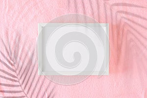 Flat lay photo of tropical leaf shadows on pink sandy background and white frame