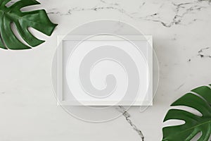 Flat lay photo of tropical leaves on light marble background and white frame