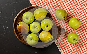 Flat lay photo - vintage wood carved bowl with apples and pears, red chequered tablecloth on black board