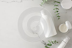 Flat lay photo of white cosmetic bottle, cream jars and eucalyptus leaves on marble background