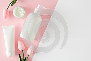 Flat lay photo of white cosmetic bottles, cream jar and spring tulips