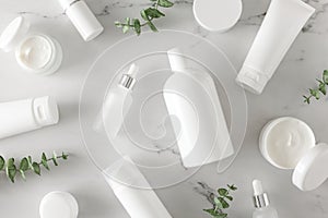 Flat lay photo of white cosmetic bottles, cream jars, dropper bottles and eucalyptus leaves