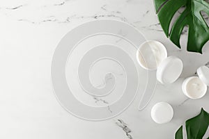 Flat lay photo of white cosmetic cream jars and green tropical leaves on marble background