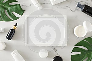 Flat lay photo of white cosmetic tubes, cream jars, amber dropper bottles and green tropical leaves