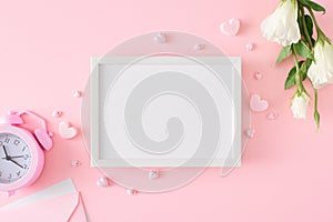 Flat lay photo of white spring flowers, pink alarm clock, envelope, hearts on pastel pink background