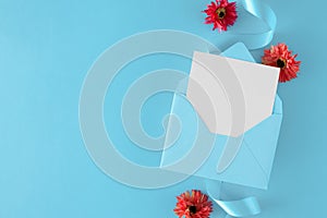 Flat lay photo woman`s day composition made of open envelope with white card, light blue silk ribbon and flowers