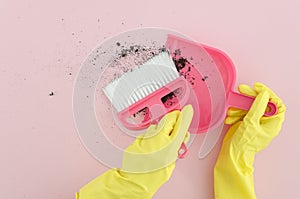Flat lay photography female hands in yellow latex gloves with brush and dustpan clean the dirt on pink background. Copy