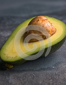 Flat lay photoshot of halved green avocado with a stone on the grey background