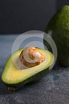 Flat lay photoshot of halved green avocado with a stone on the grey background