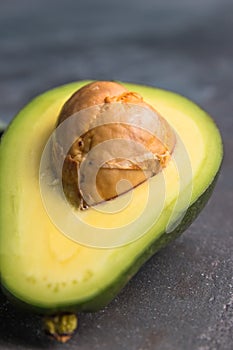 Flat lay photoshot of halved green avocado with a stone on the grey background