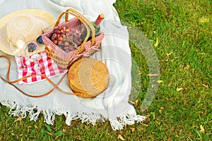 Flat lay Picnic on a green lawn, with a plaid picnic basket and a bottle of wine and glasses, a handbag and a hat with space.