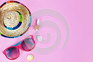 Flat lay with pink sunglasses for children and colorful straw hat and sea shells on pink background with blank copy space