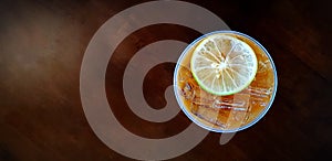 Flat lay of plastic glass of iced lemon tea with sliced lime or lemon on top isolated on dark wooden background