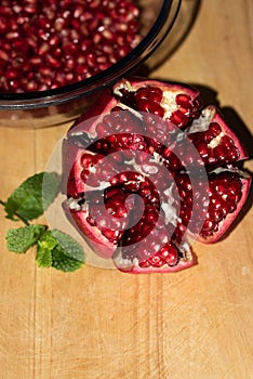 Flat lay pomegranate displayed on wooden board next to a mint leaf and sequence of bawl of seeds