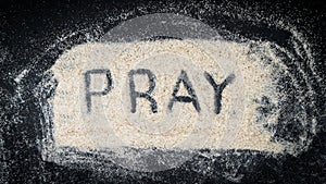 Flat lay of PRAY text written on white sand