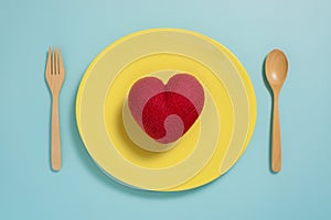 Flat lay of red heart on yellow plate with fork on pastel blue color background