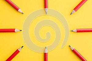 Flat lay of red pencils around border frame on yellow background with copy space. Education, learning and back to school concept