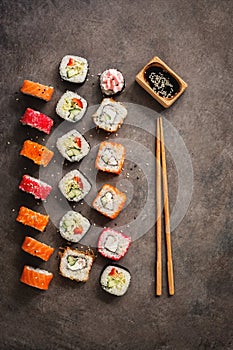 Flat lay rows of sushi rolls, soy sauce and chopsticks on a dark rustic background. View from above. Traditional asian food
