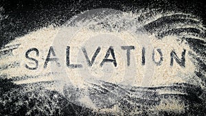 Flat lay of SALVATION word written on white sand photo