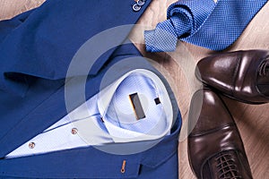 Flat lay set of classic mens clothes such as blue suit, shirts, brown shoes, belt and tie on wooden background.