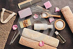 Flat lay a set of various bath accessories. Terry towel, soap, comb, oil, shampoo, loofah washcloth, sea salt on a dark rustic