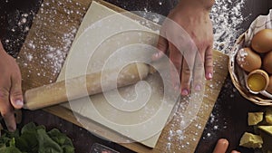 Flat lay shot: chef rolls out the dough with a rolling pin on the kitchen table, table top of the rolling out the puff