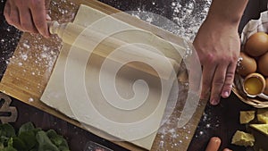 Flat lay shot: chef rolls out the dough with a rolling pin on the kitchen table, table top of the rolling out the puff