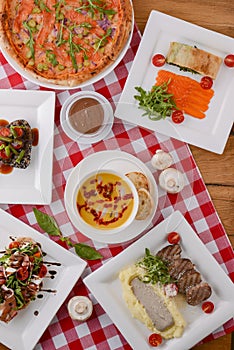 Flat lay shot of delicious italian cuisine. Delicious pizza, salmon rolls, pumpkin soup and salad on a wooden table