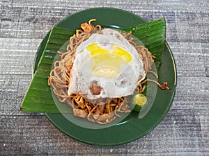 Flat lay shot a fried noodles or mee goreng mamak with fried egg on top on wooden background.