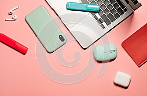 Flat lay shot with a silver grey laptop with a black keyboard, wireless turquoise computer mouse, earphones, smartphone in a light