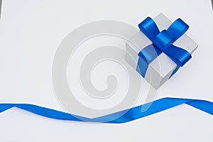 Flat lay silver gift box with blue satin bow ribbon on white background