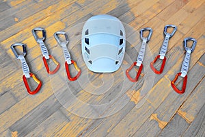 Flat lay of six quickdraws with solid gate carabiners and white helmet, on wooden background - top down view. Space for text.