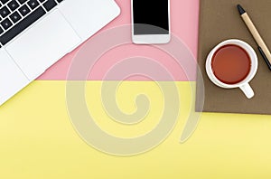 Flat lay of smart phone, laptop, notebook, pen and a cup of coffee with copy space on pastel yellow and pink background.