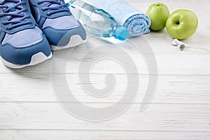 Flat lay sport shoes, bottle of water, apples, towel and earphones on white wooden background. Sport equipment. Healthy lifestyle