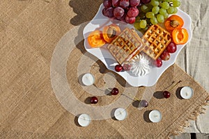 Flat lay, still life and food photo. A plate with fruits and waffles stands on a burlap