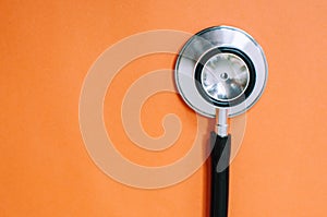 A flat lay still life of stethoscope on an orange background with copy space