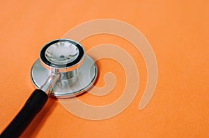 A flat lay still life of stethoscope on an orange background with copy space