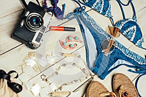 Flat lay of summer fashion with blue bikini swimsuit, camera and other girl accessories on white wooden background
