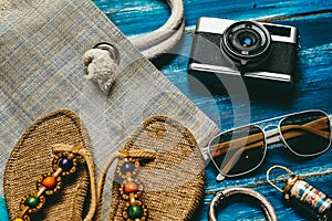 Flat lay of summer fashion with camera slippers sunglasses and other girl accessories on blue wooden background
