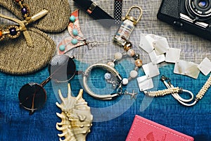 Flat lay of summer fashion with camera, slippers, sunglasses and other girl accessories on top of the bag as background