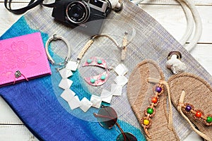 Flat lay of summer fashion with camera, slippers, sunglasses and other girl accessories on top of the bag on white wooden backgrou