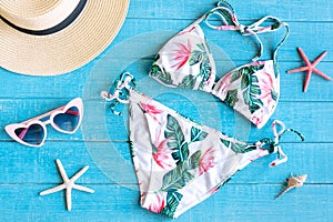 Flat lay of summer items with colorful bikini, sunglasses, straw hat, and coral on blue wooden background, top view. Summer