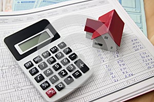 Flat lay of a table on which there is a calculator, a little house on top of the economic expenses of a home