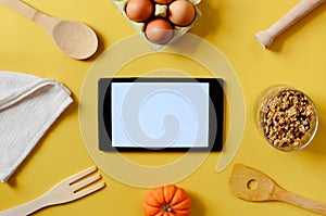 Flat lay with tablet with white mockup and place for text on yellow background. Food blogger`s workplace. Culinary blog, recipes