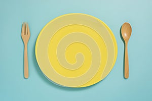 Flat lay of tableware, yellow plate and fork on pastel blue colo