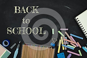 Flat lay tationery, notepads, pencils and clips over classroom blackboard with white chalk sign. Back to school concept