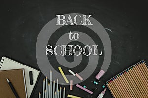 Flat lay tationery, notepads, pencils and clips over classroom blackboard with white chalk sign. Back to school concept